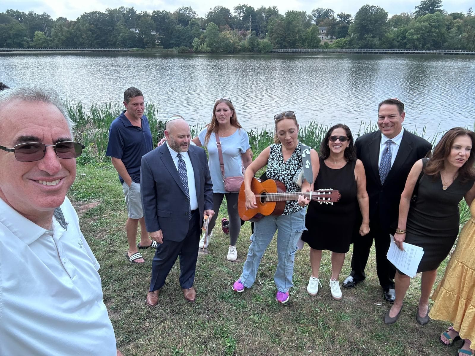TBS community gathered by the lake for Tashlich with guitar player in a beautiful outdoor setting