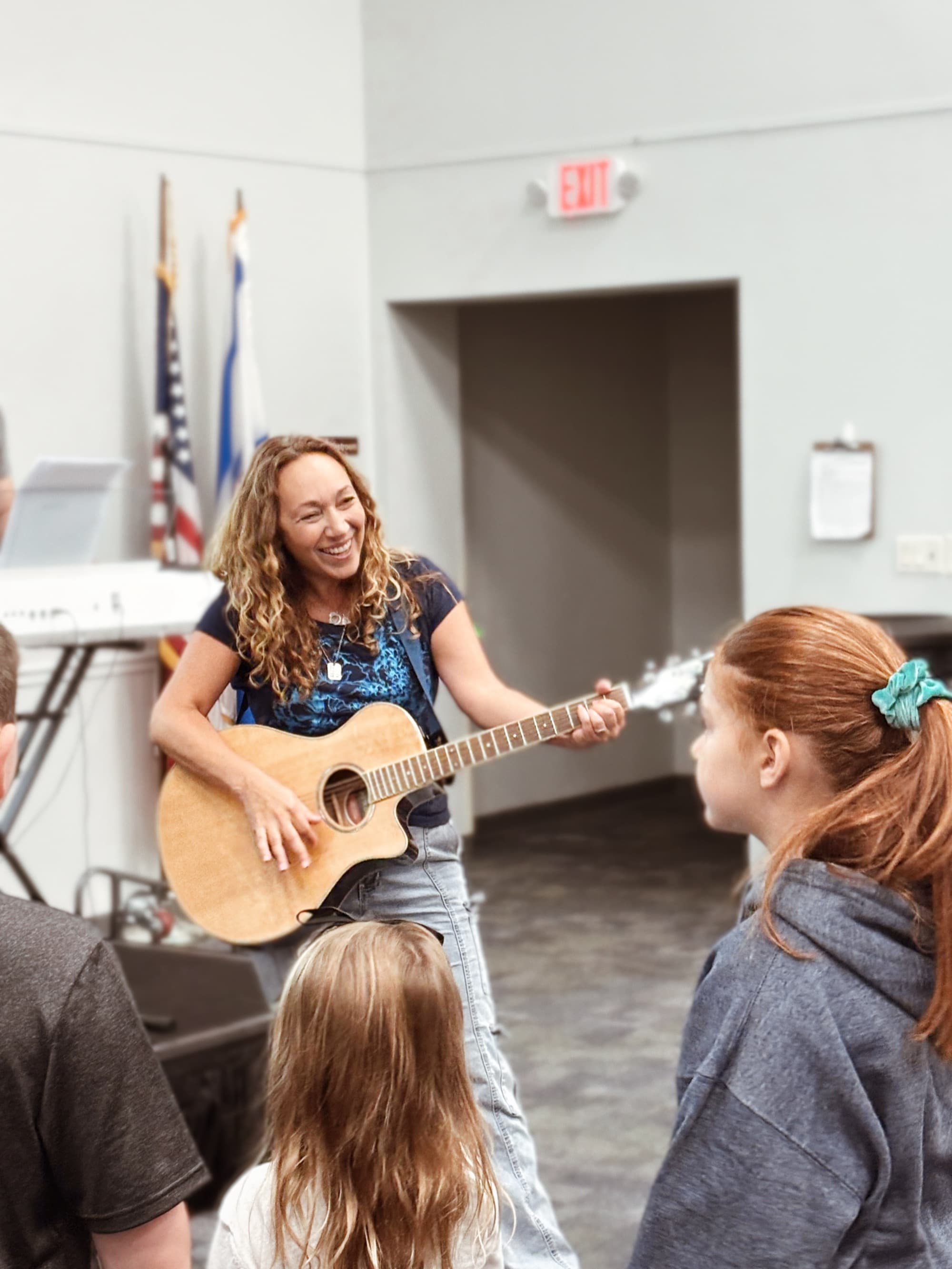 Cantor Anna smiling warmly with guitar surrounded by children