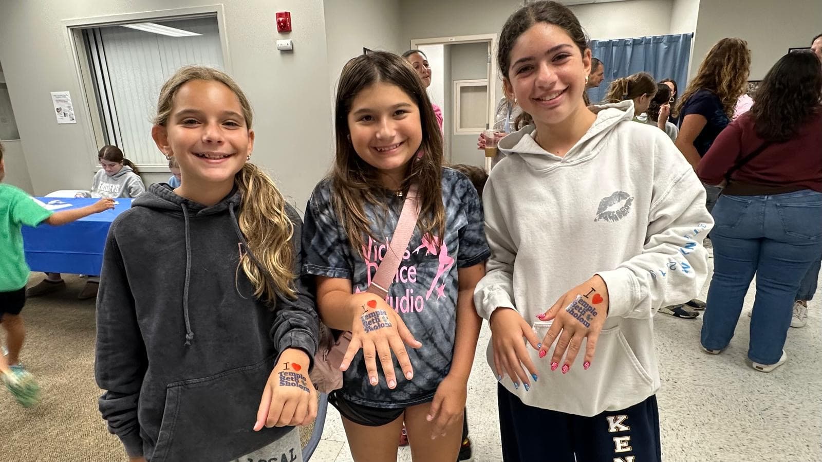Three smiling girls showing off their 'I love Temple Beth Sholom' hand stamps
