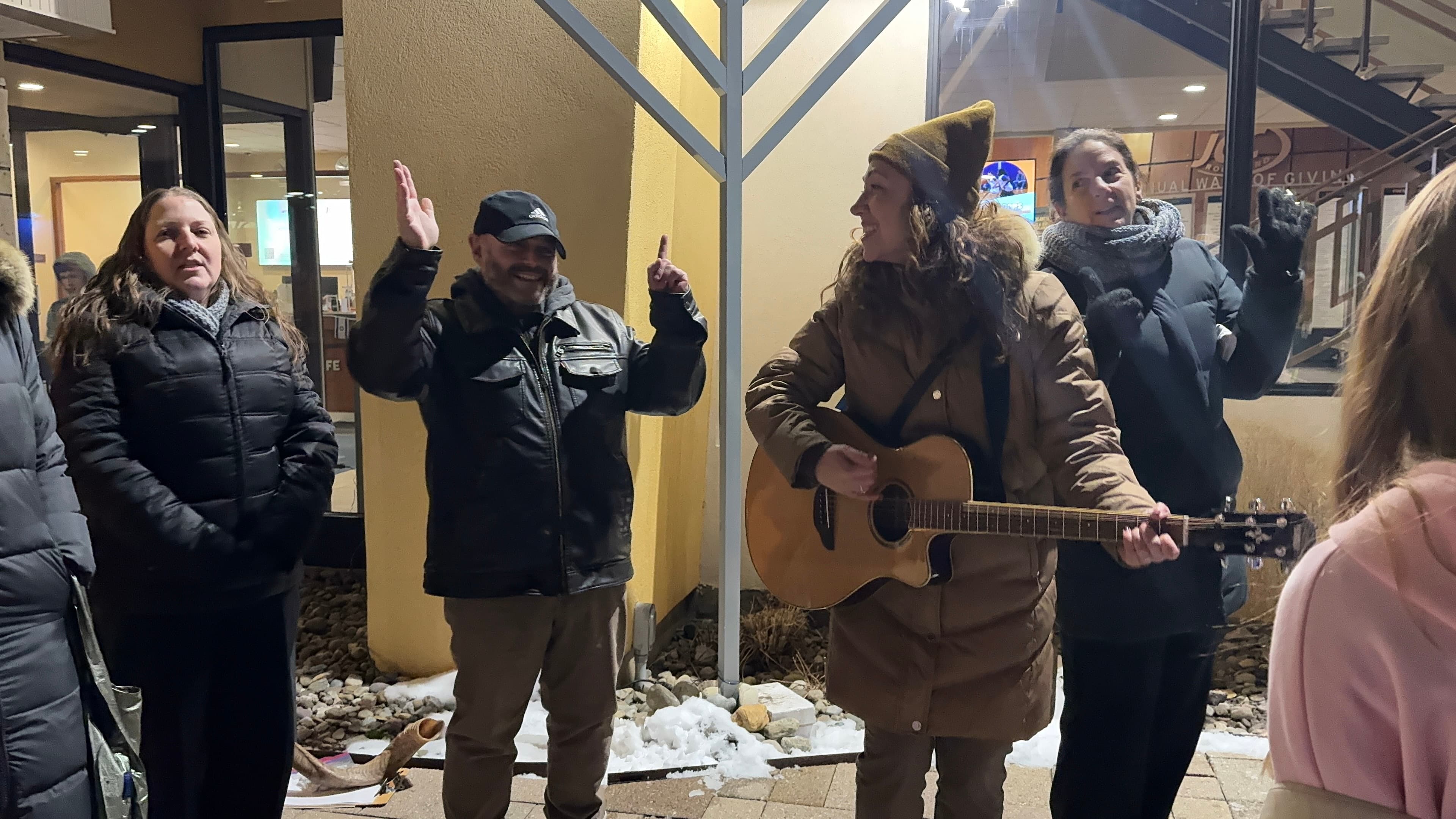 Community gathered outdoors for Hanukkah menorah lighting with guitar